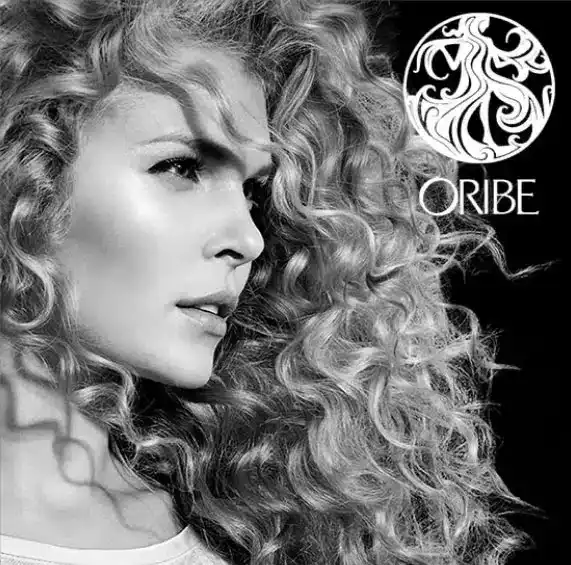 Woman with voluminous curly hair and ORIBE logo in black and white.