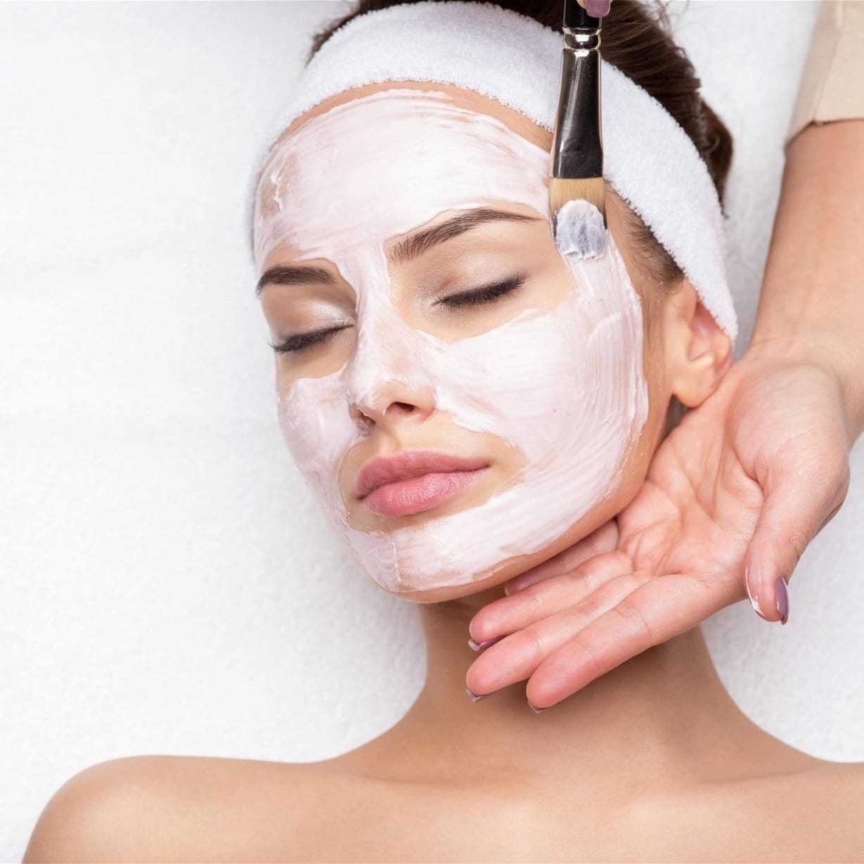 Woman receiving a facial mask treatment at a spa, eyes closed and relaxed.