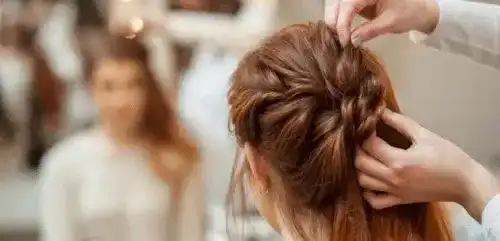 Hair stylist braiding a woman's hair in a salon setting.