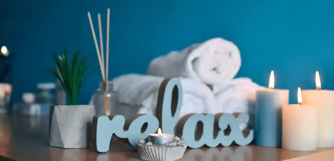 Cozy spa setting with candles, towels, and relax sign on a wooden table.