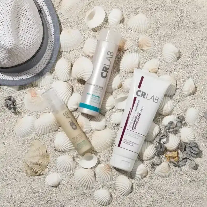 CRLAB hair products on sandy beach surrounded by seashells and a sunhat.